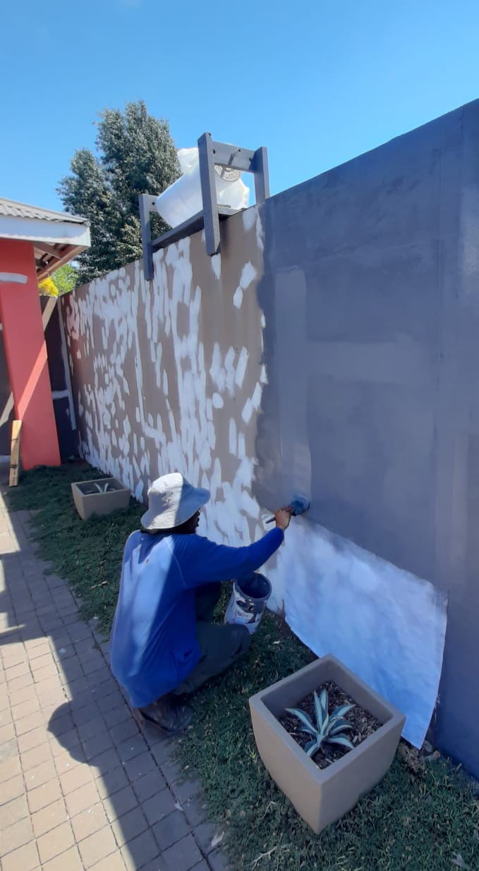 A worker painting the wall with dark grey liquid rubber waterproofing